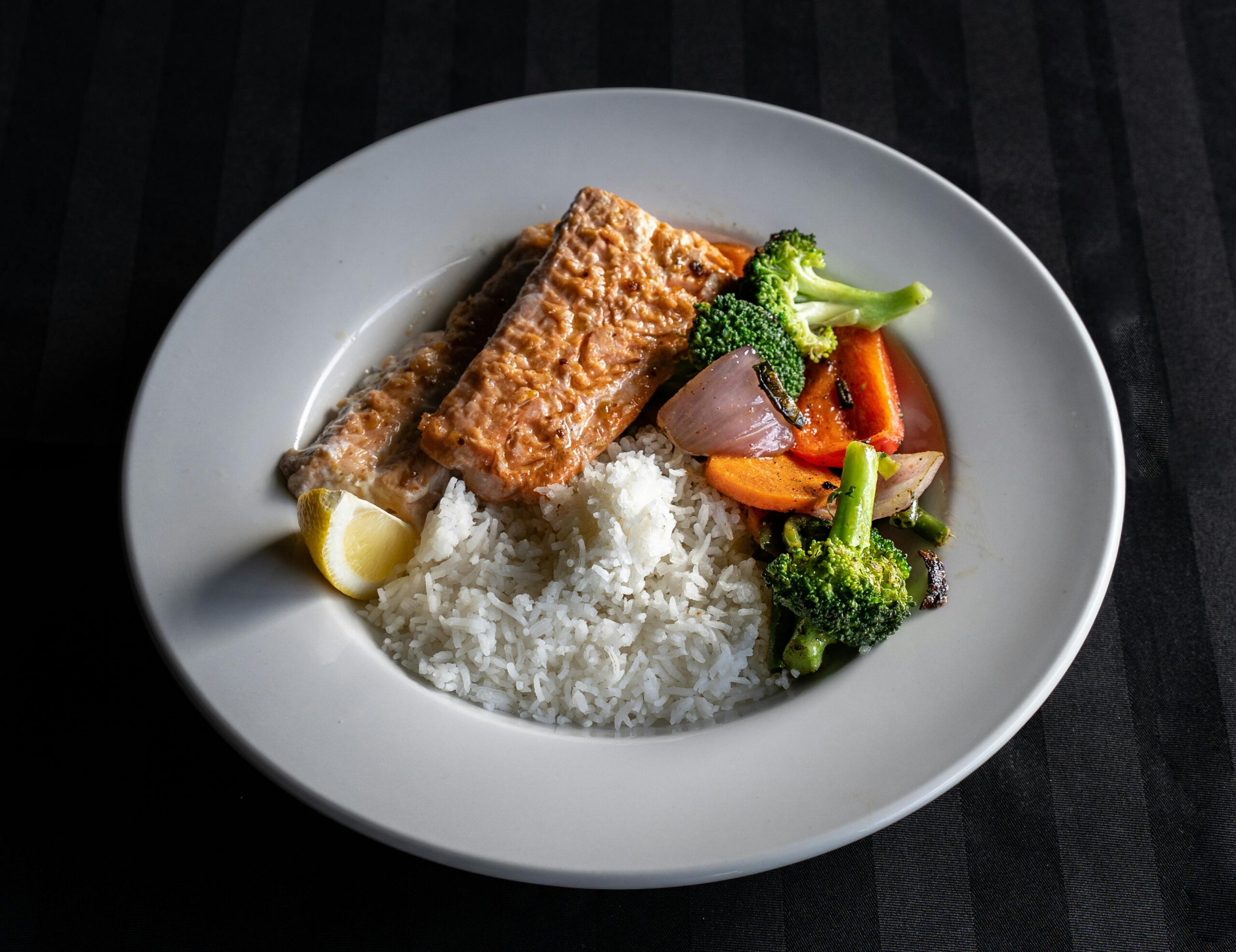 A beautifully plated salmon dish with rice, broccoli, and vegetables on a ceramic plate.