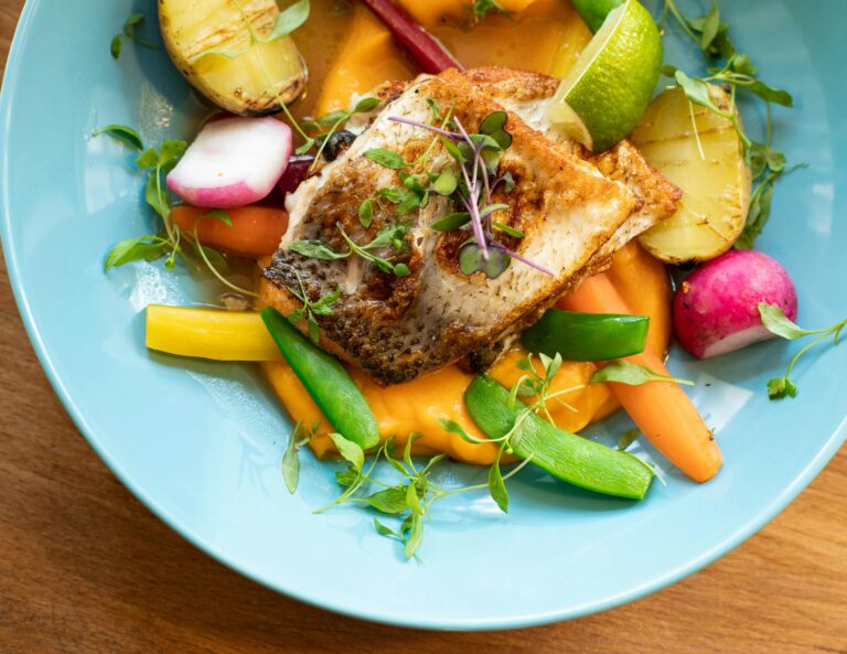 Colorful salmon dish with fresh vegetables on a blue plate, perfect for gourmet cuisine lovers.