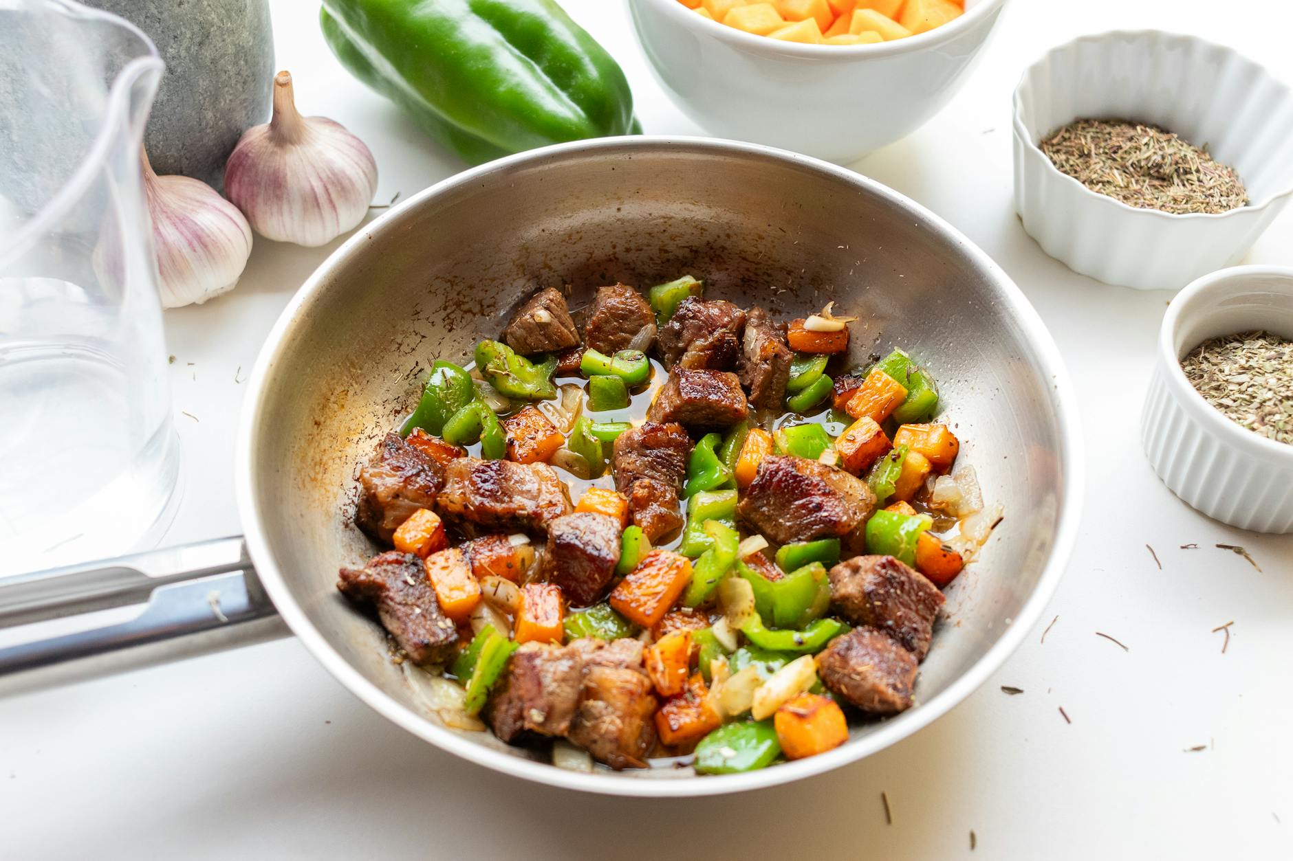 Delicious beef stir fry with bell peppers and carrots in a stainless steel pan, seasoned with herbs.